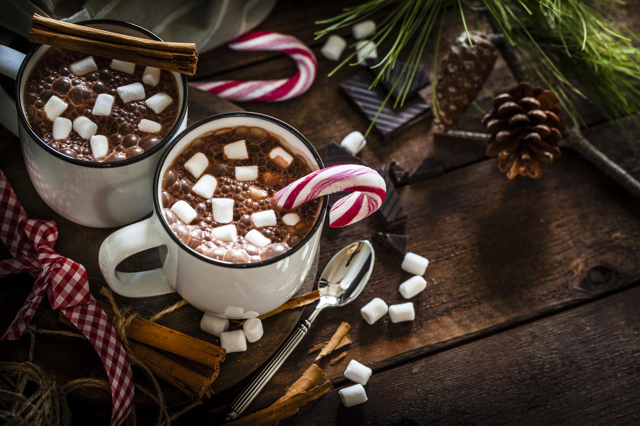 Two homemade hot chocolate mugs with marshmallows on rustic wooden Christmas table